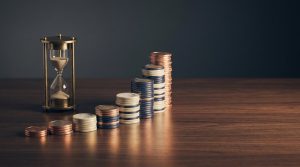 Qué es el interés compuesto y cuánto cambia a 20 años: montones de monedas cada vez más altos junto a un reloj de arena