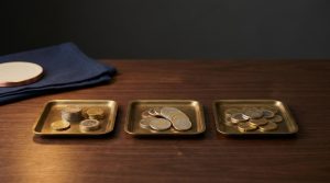 MyInvestor vs Trade Republic vs DEGIRO: costes comparados: tres bandejas de latón con monedas para comparar